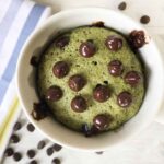 keto matcha mug cake in a white mug topped with unsweetened chocolate chips.