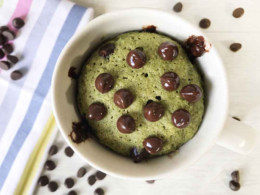 keto matcha mug cake in a white mug topped with unsweetened chocolate chips.