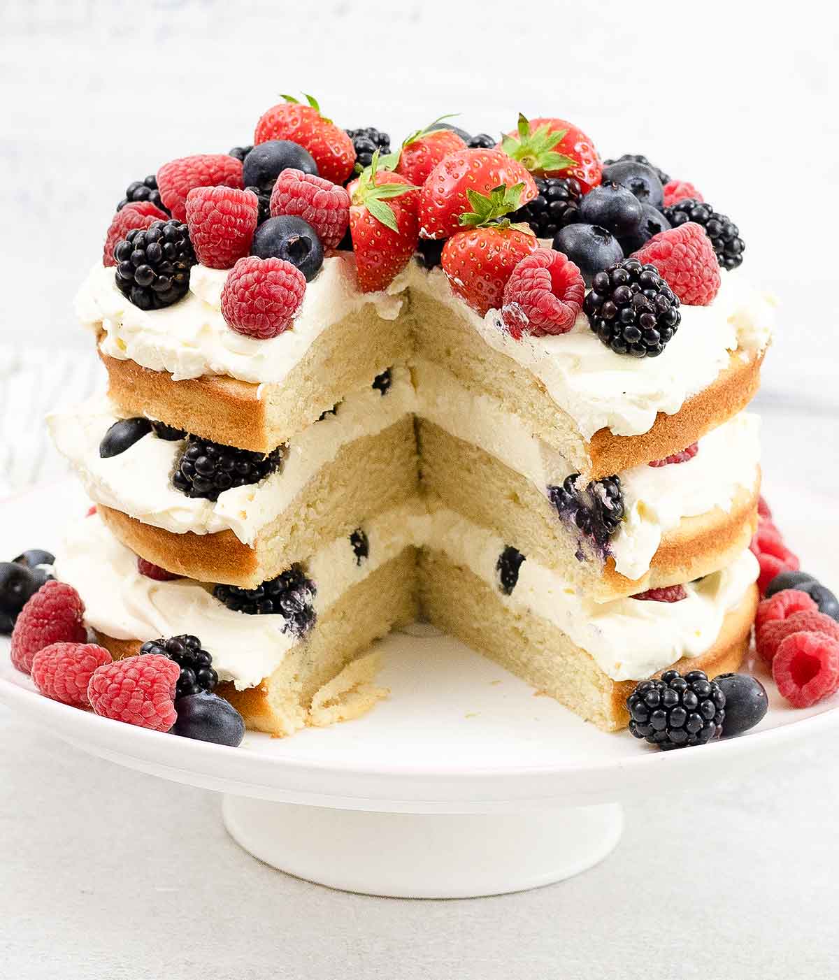 Mixed berry cake and some berries around in a cake stand.