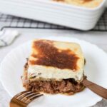 A slice of Moussaka in a serving plate showing the eggplant, meat and bechamel layers.