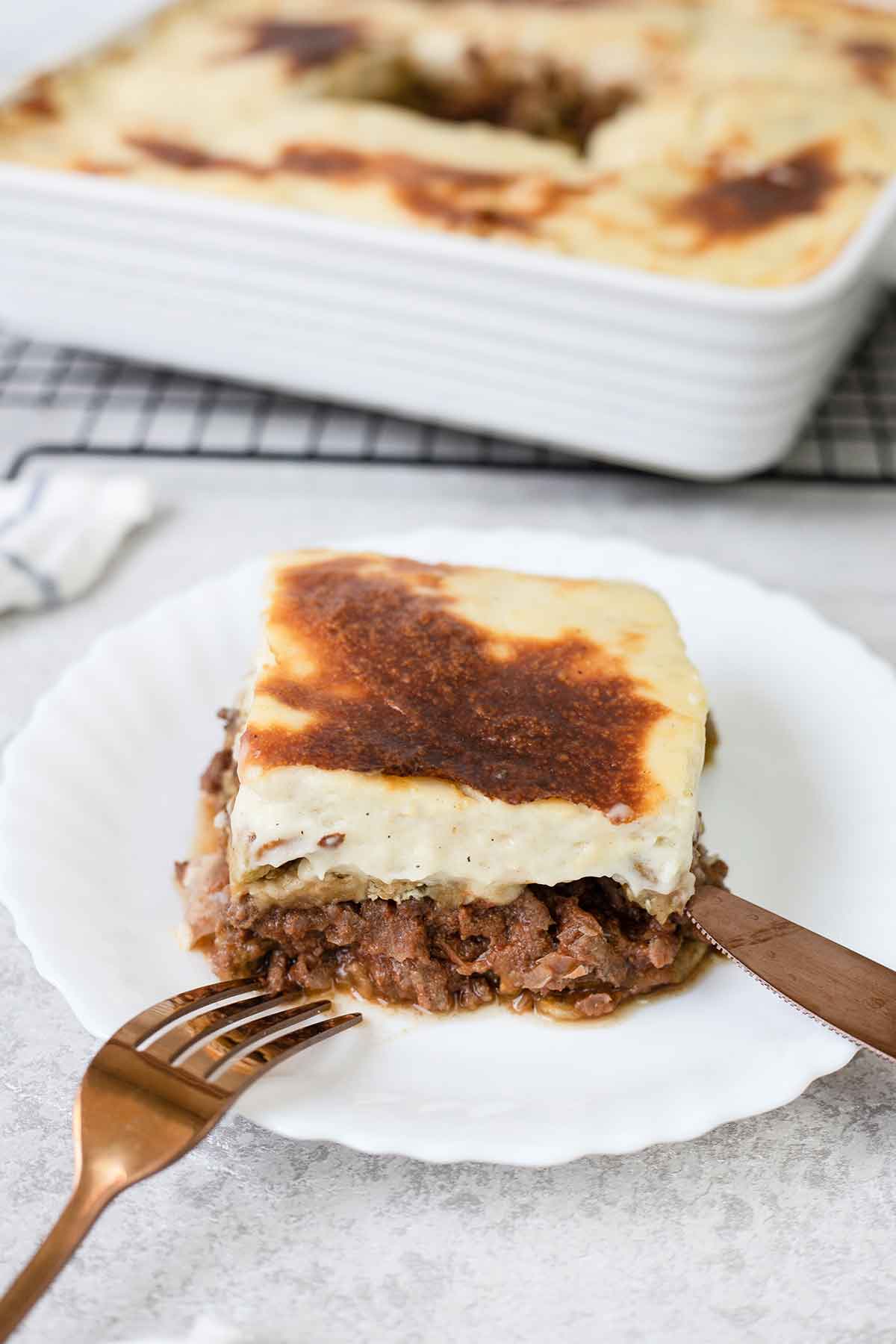 A slice of Moussaka in a serving plate showing the eggplant, meat and bechamel layers.