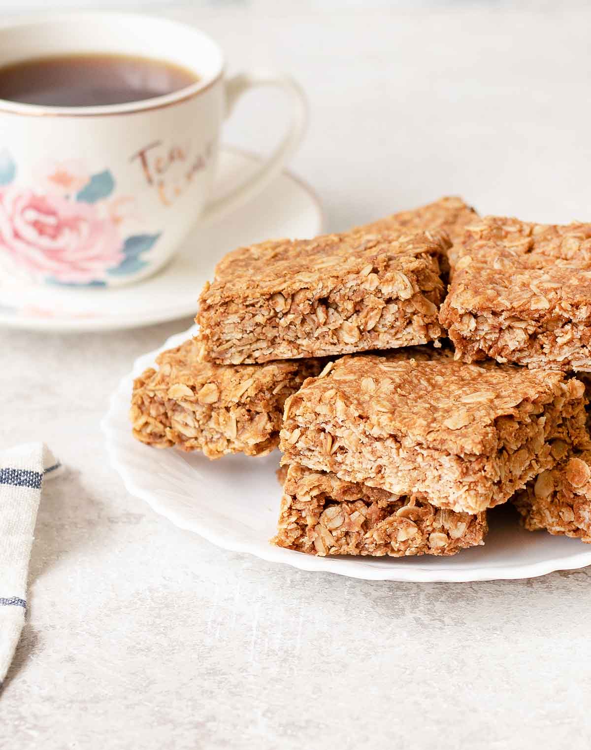 Peanut butter flapjacks bars are in a plate and a cup of tea in the background.