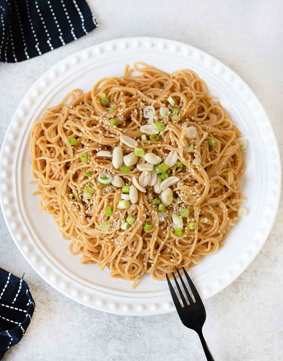 Sesame Peanut Noodles in a serving plate topped with sesame seeds, green onion and peanuts.