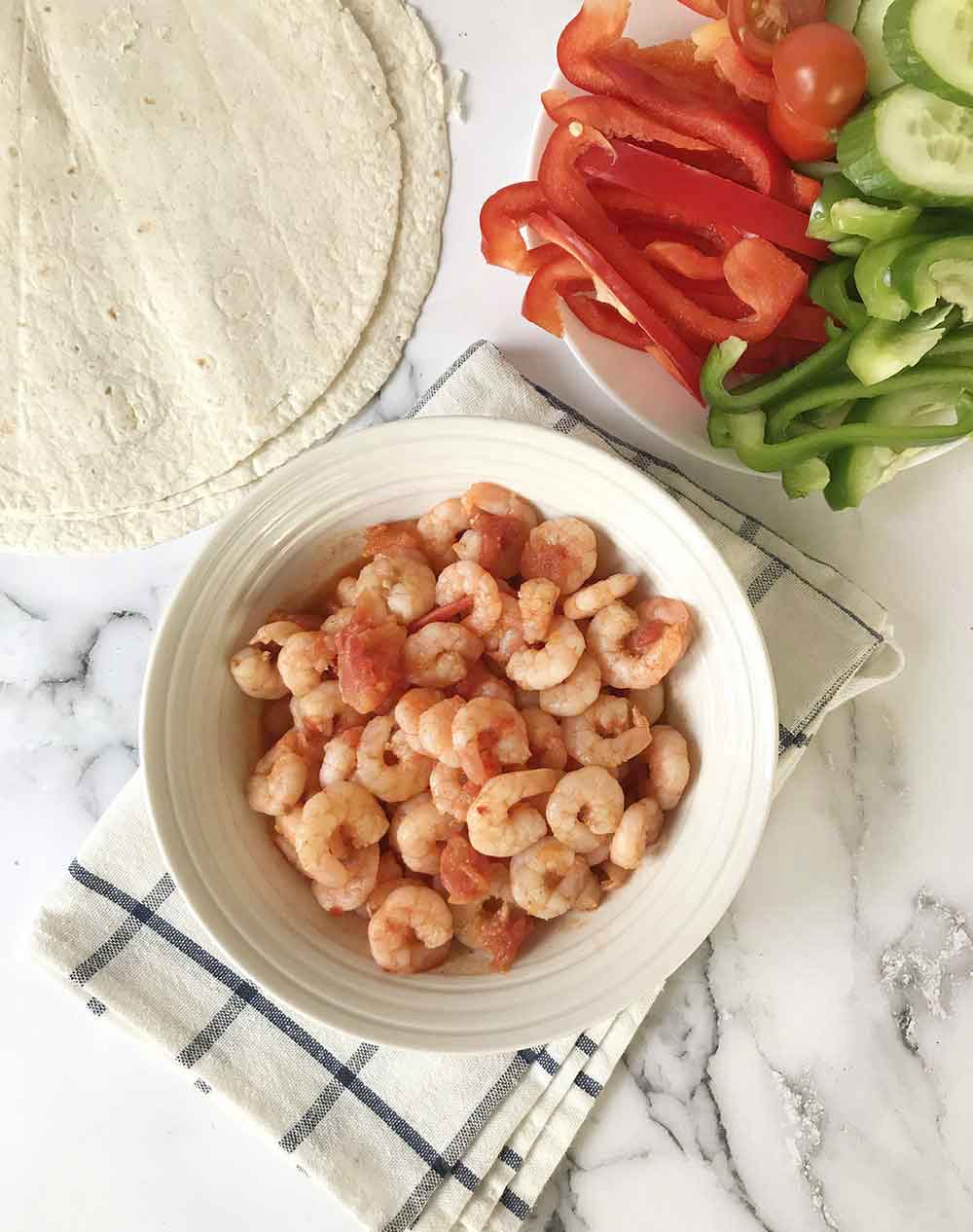 Spicy shrimp in tomato sauce in a bowl, a plate of veggies and some tortilla.