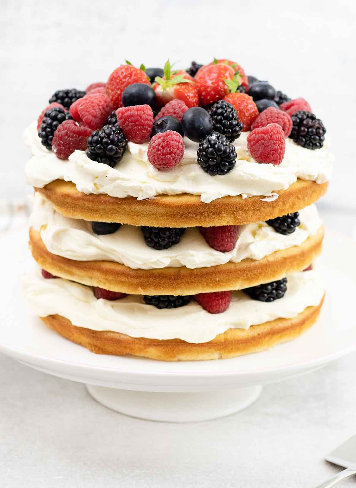 fresh berry and whipped cream layer cake on a cake stand.