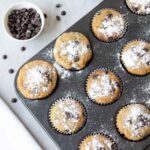 banana muffins with chocolate chips in a muffin tin and some chocolate chips in a bowl.