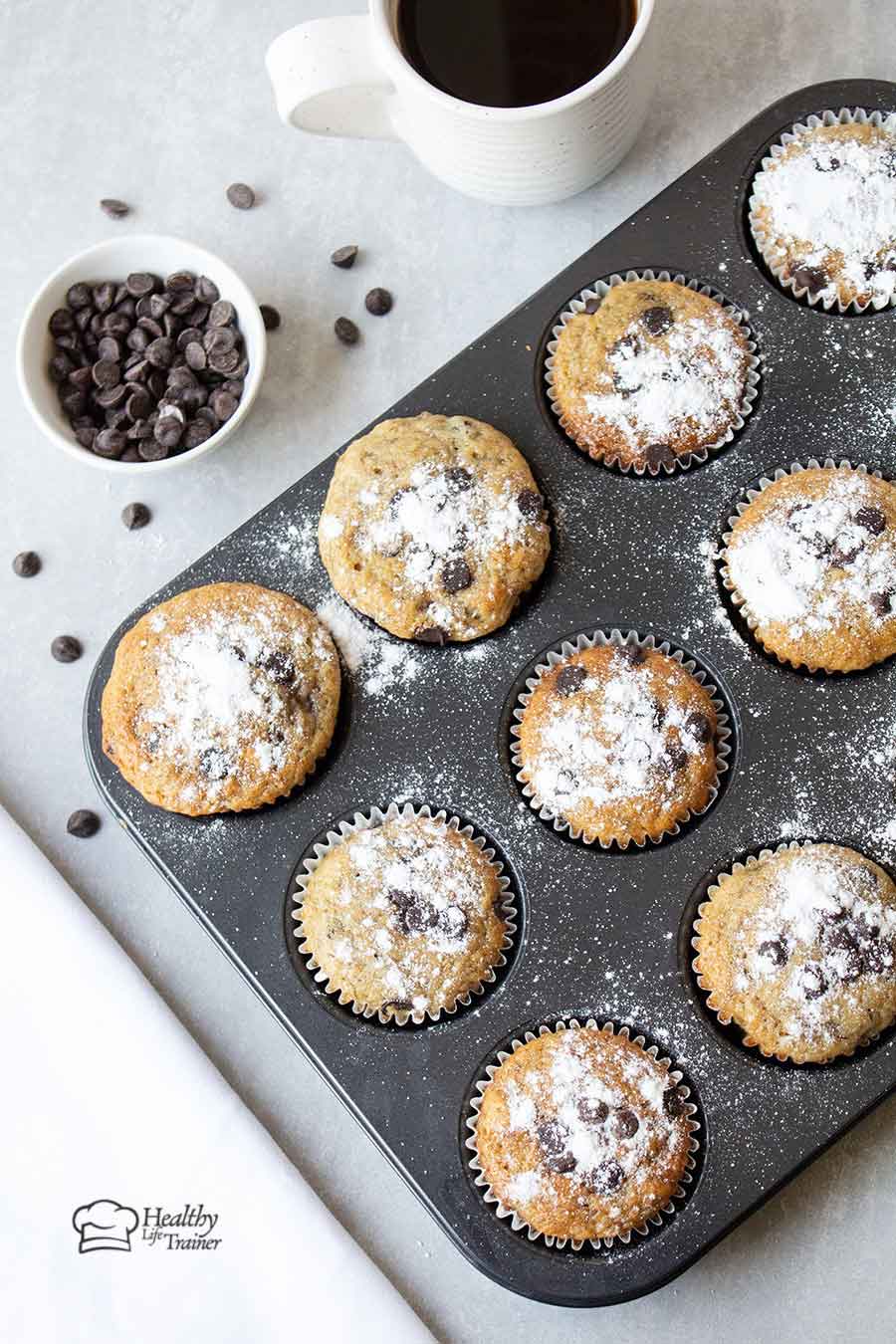 banana muffins with chocolate chips in a muffin tin and some chocolate chips in a bowl.