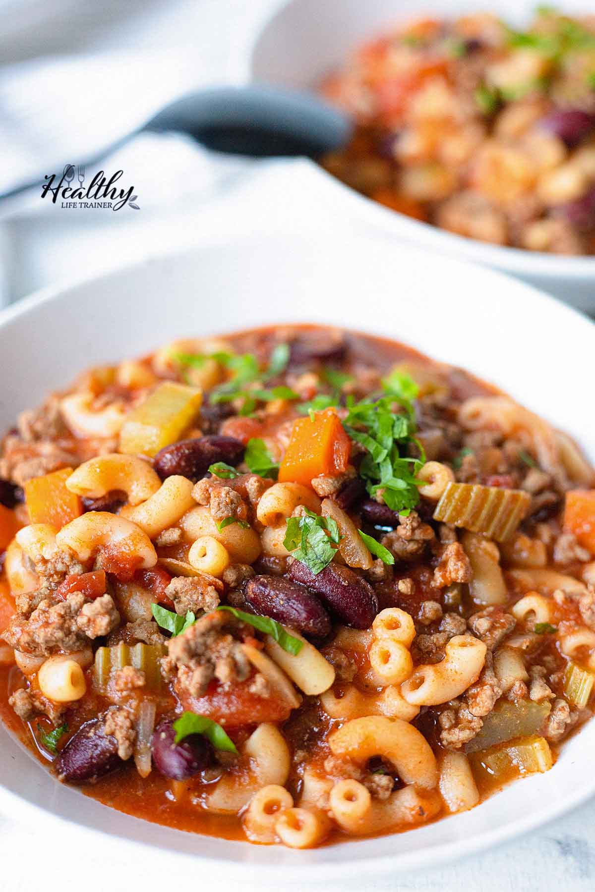 A big bowl of beef and macaroni soup with veggies and beans.