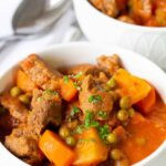 beef stew with potatoes, carrots and peas in a white bowl.