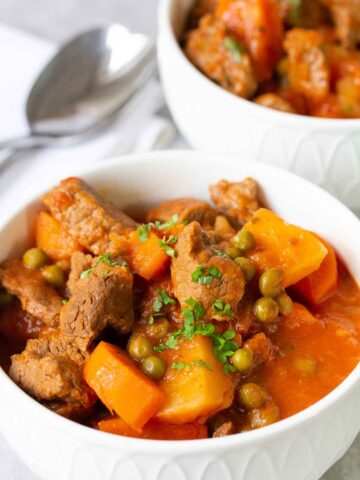 beef stew with potatoes, carrots and peas in a white bowl.