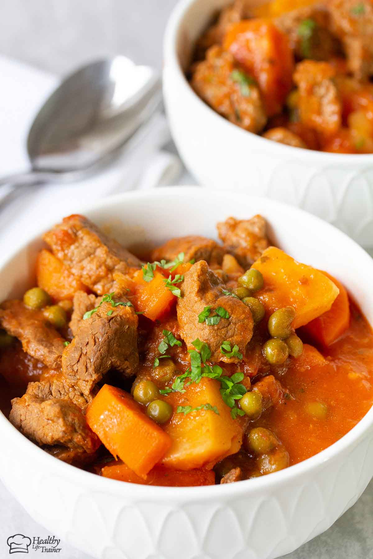 beef stew with potatoes, carrots and peas in a white bowl.