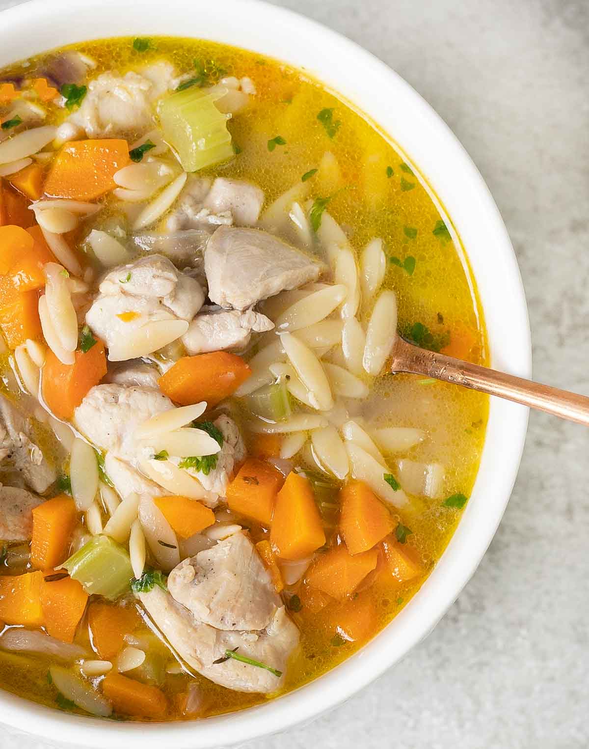 A spoon in a bowl full of lemon chicken orzo soup.