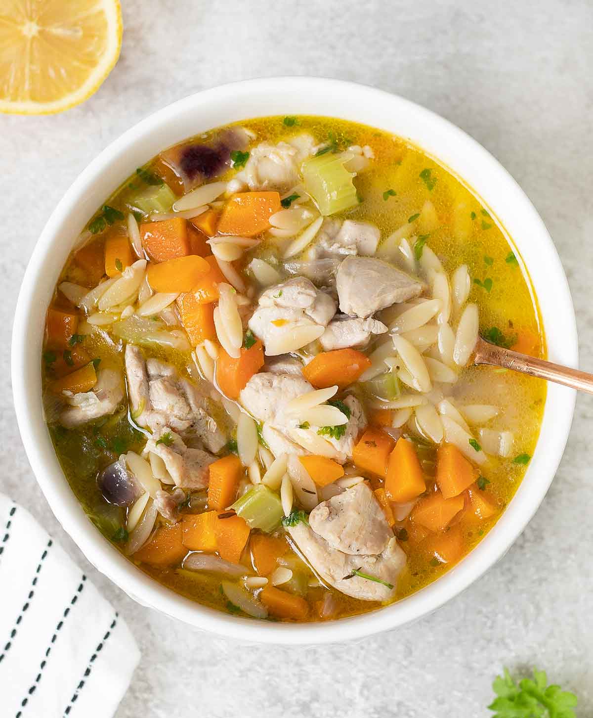 A bowl of lemon chicken orzo soup and half of a lemon in the background.