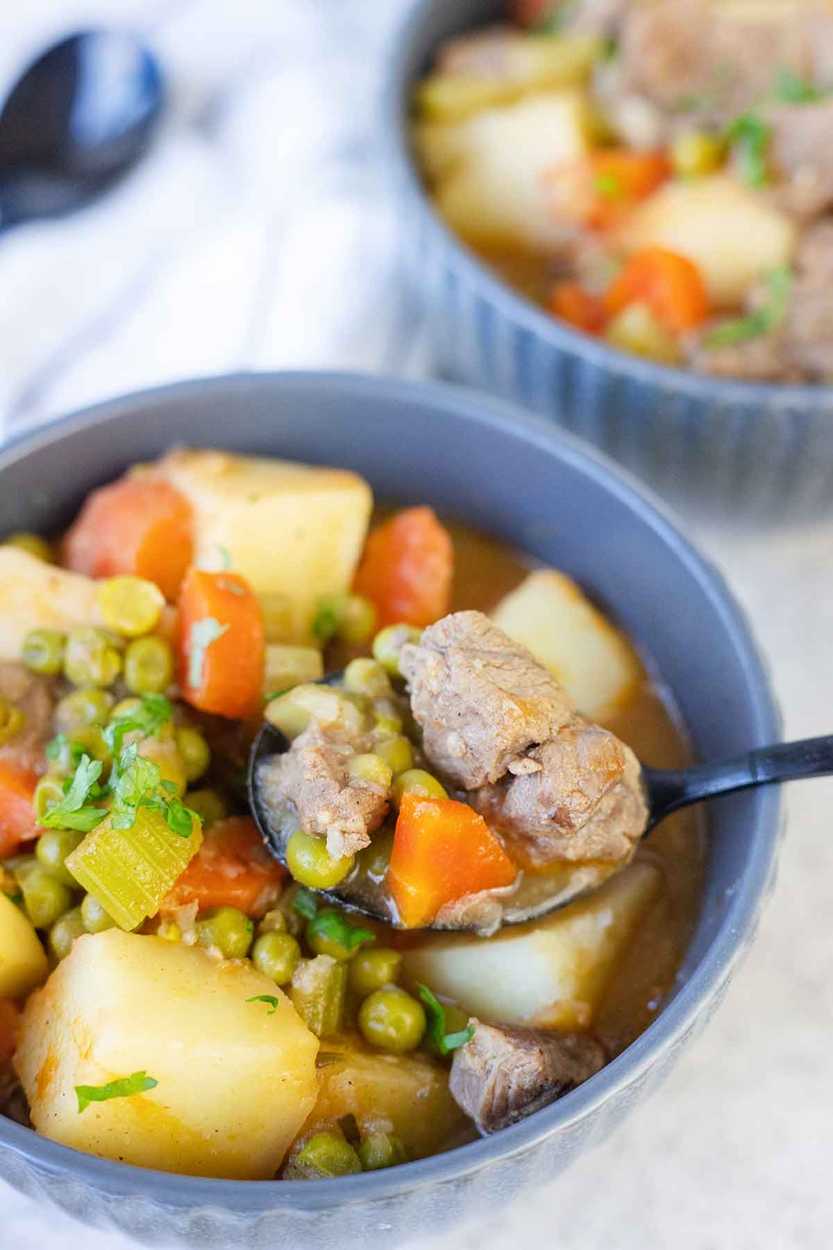 A spoonful of lamb stew made with potatoes, peas, celery and carrots.