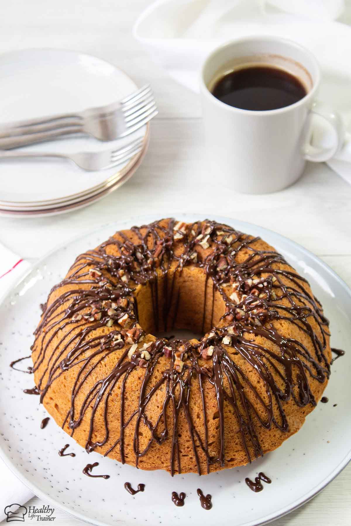 A whole sweet potato pound cake on a serving plate and a cup of coffee is in the background.