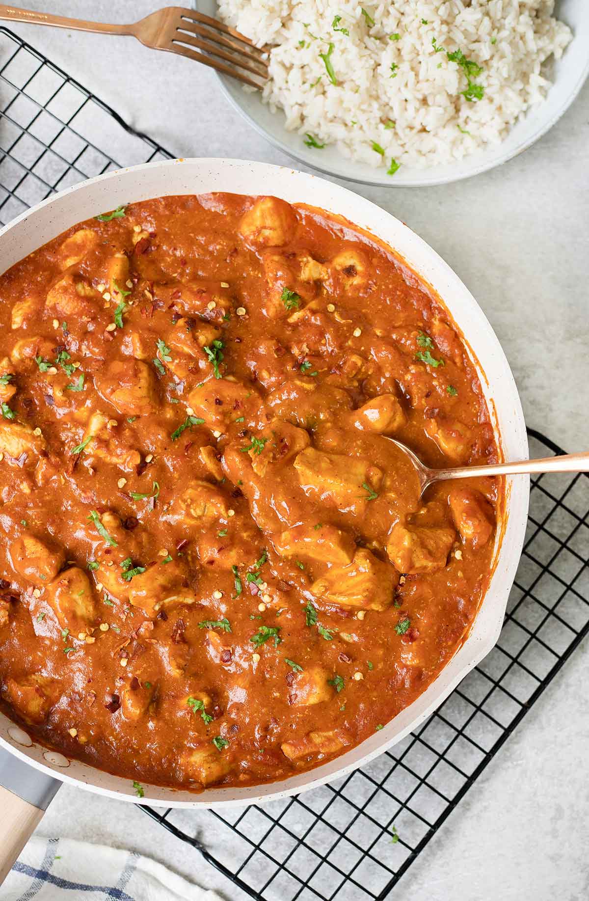 A large pan full of Indian chicken curry and a bowl of white rice in the background.