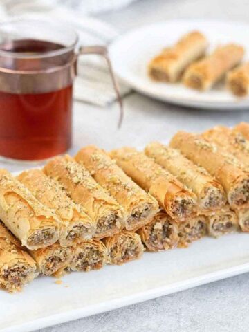 a plate full of Baklava Rolls and a cup of tea is in the background.