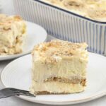 Banana pudding lasagna topped with fresh slices of banana and biscuit crumbs.