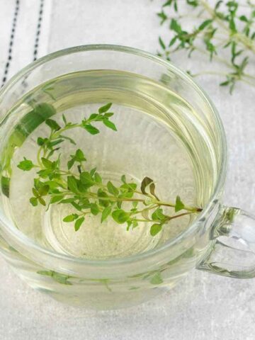 Thyme Tea in a cup and a few springs of fresh thyme are in the background.