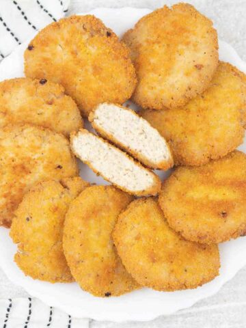 Crispy chicken patties on a plate, one of them cut in half.