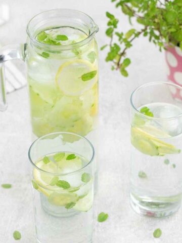 Cucumber Water in a glasses flavored with lemon slices and mint leaves.