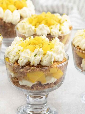 kunafa with mango and cheesecake in cups topped with whipped cream.