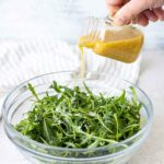 Pouring the Lemon Mustard Vinaigrette over a rocket salad.