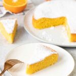 Orange Polenta Cake topped with powdered sugar and half an orange is in the background.