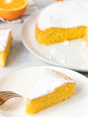 Orange Polenta Cake topped with powdered sugar and half an orange is in the background.