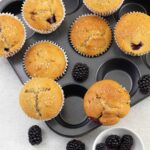 Blackberry Muffins on a muffin tin and some fresh blackberries around them.