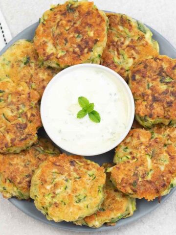 courgette fritters around a small bowl of yogurt dip.