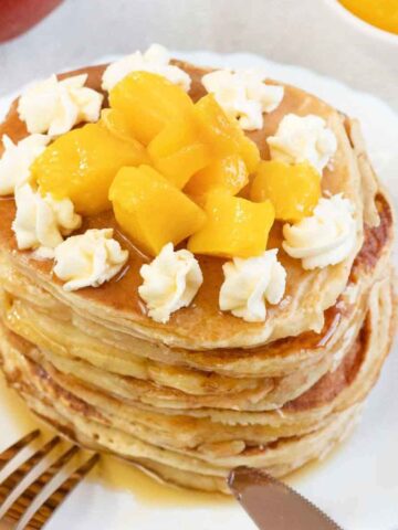 Mango pancakes topped with fresh mango chunks and whipped cream.