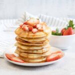 A stack of Oat Milk Pancakes topped with fresh strawberry slices.