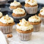 carrot cake cupcakes topped with cream cheese frosting and walnuts.