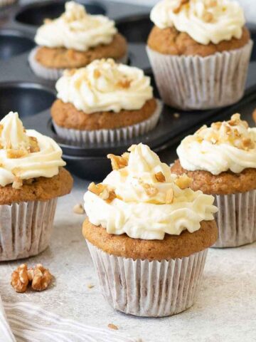 carrot cake cupcakes topped with cream cheese frosting and walnuts.
